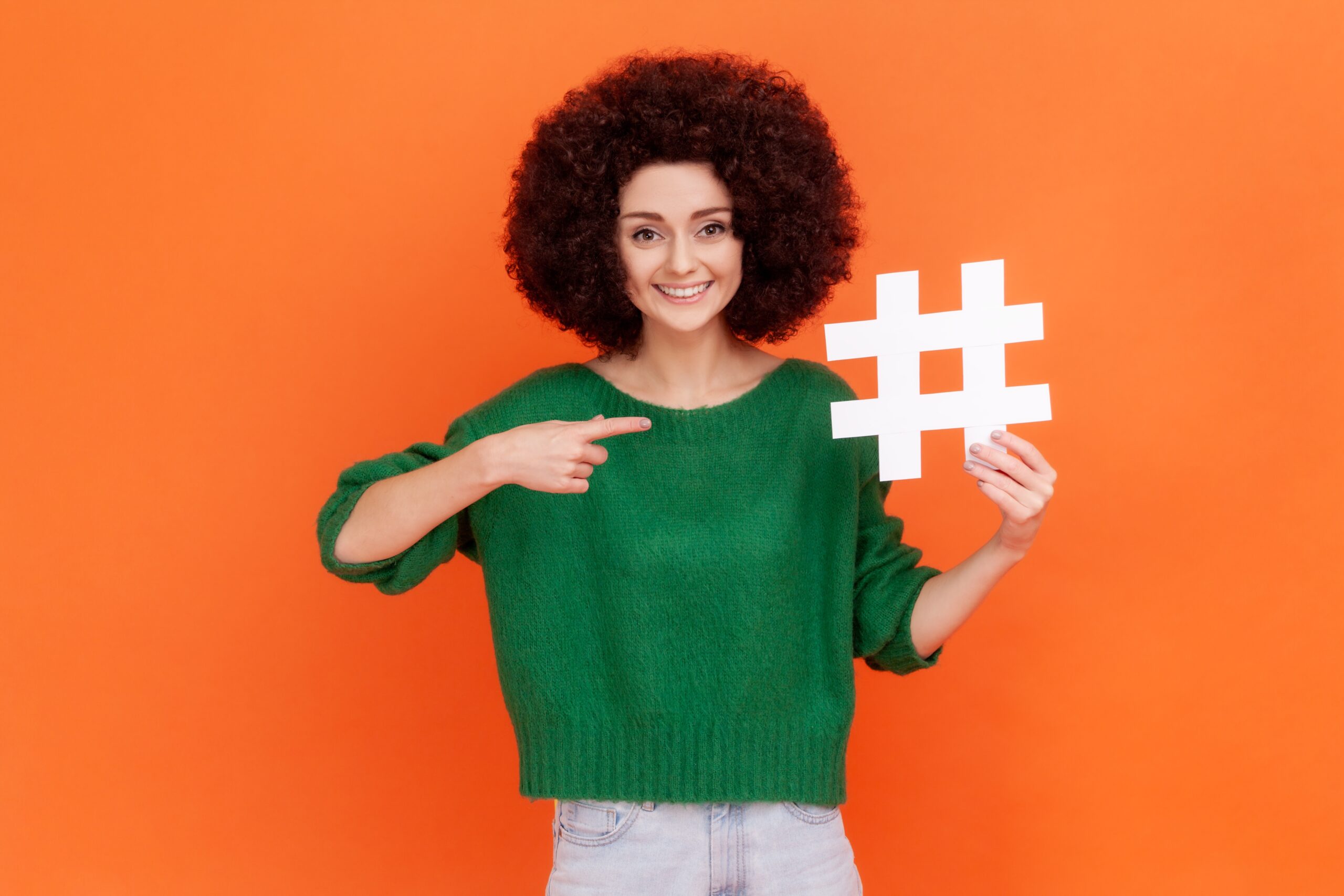 A lady pointing to a hashtag sign she is holding up
